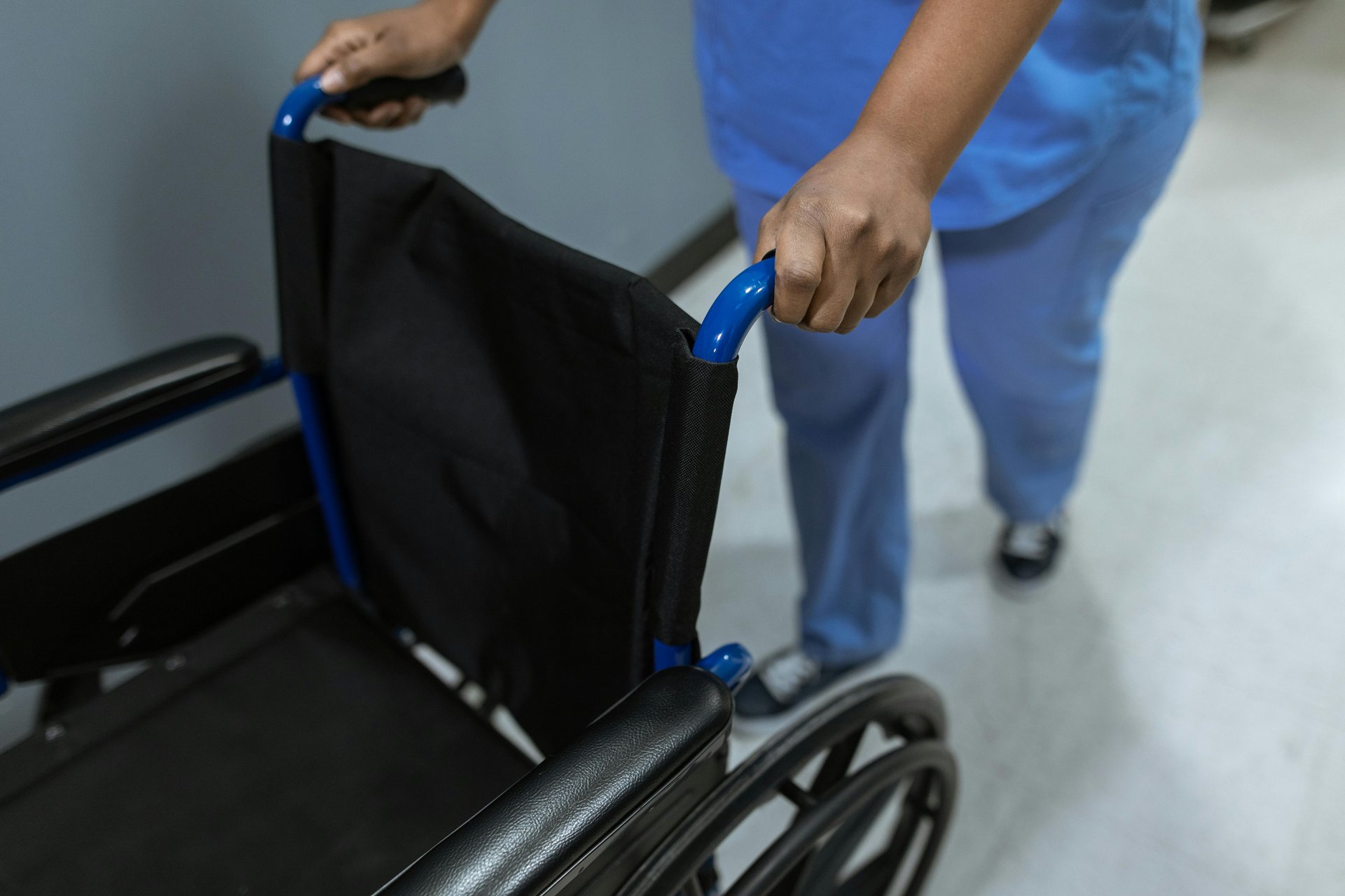 Disability support worker in scrubs pushing a wheelchair in a healthcare setting, representing NDIS provider services