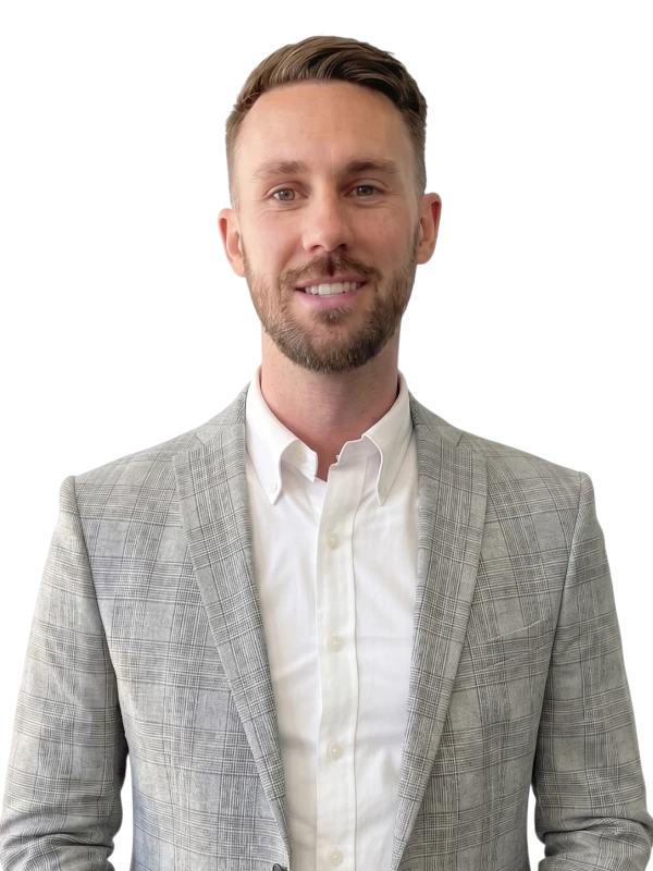 Ben Pym wearing a light gray plaid suit jacket over a white button-up shirt, standing and smiling at the camera against a plain background.