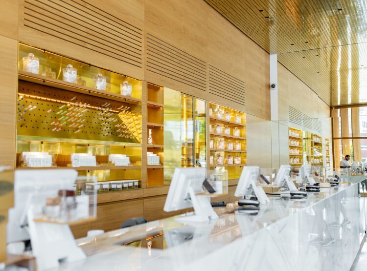 A modern, well-lit pharmacy interior with white countertops, multiple checkout counters, and shelves stocked with various products behind the counter.