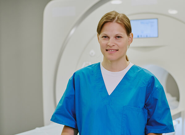 A healthcare professional in blue scrubs stands in front of an MRI machine in a medical facility.