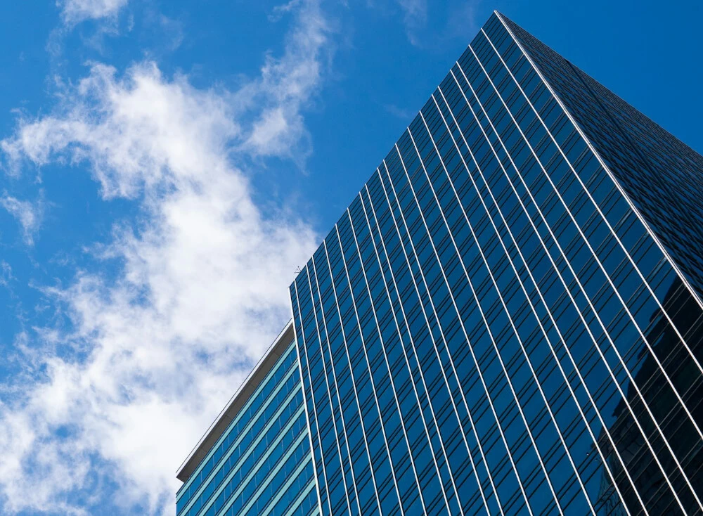 Glass skyscraper with grid-like facade against a blue sky with scattered clouds, viewed from a low angle.
