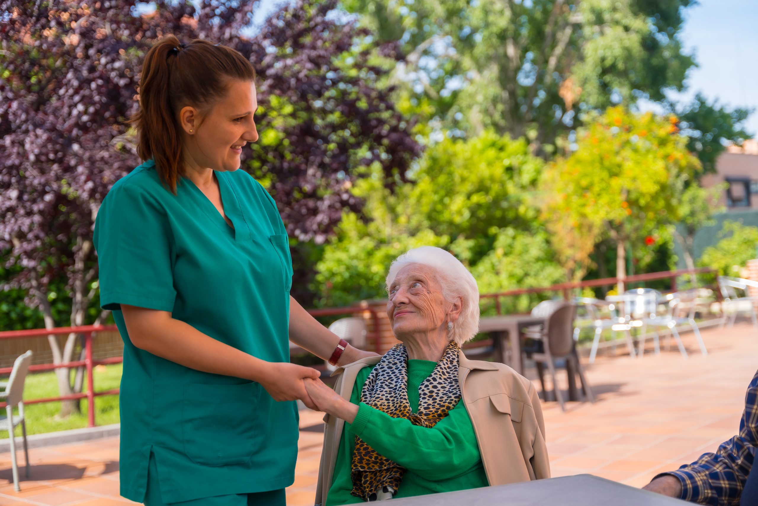 Nurse providing compliant aged care services to elderly woman in garden setting