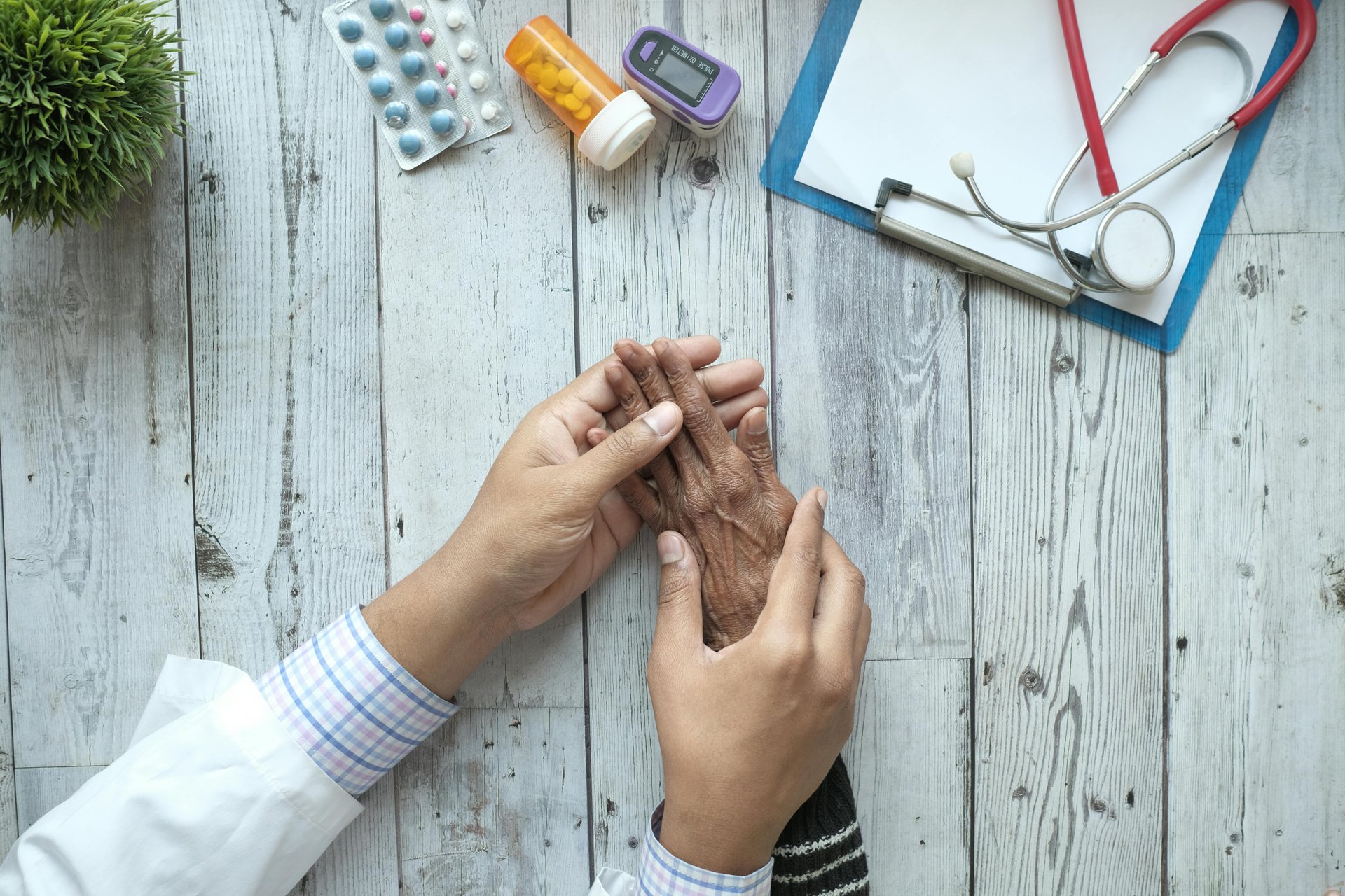 Doctor holding elderly patient hands on a desk with medication and stethoscope