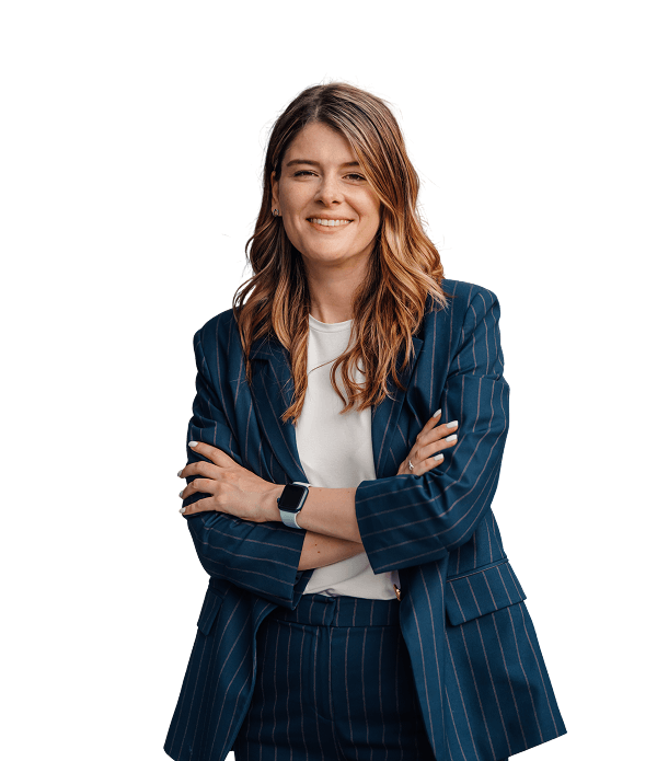 A woman with long brown hair wearing a pinstripe suit and white shirt stands with arms crossed, smiling against a plain white background.