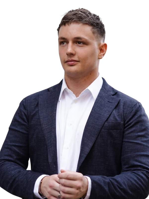Kyle Hunt in a white dress shirt and dark blazer stands with hands clasped, looking slightly to the side against a plain background.
