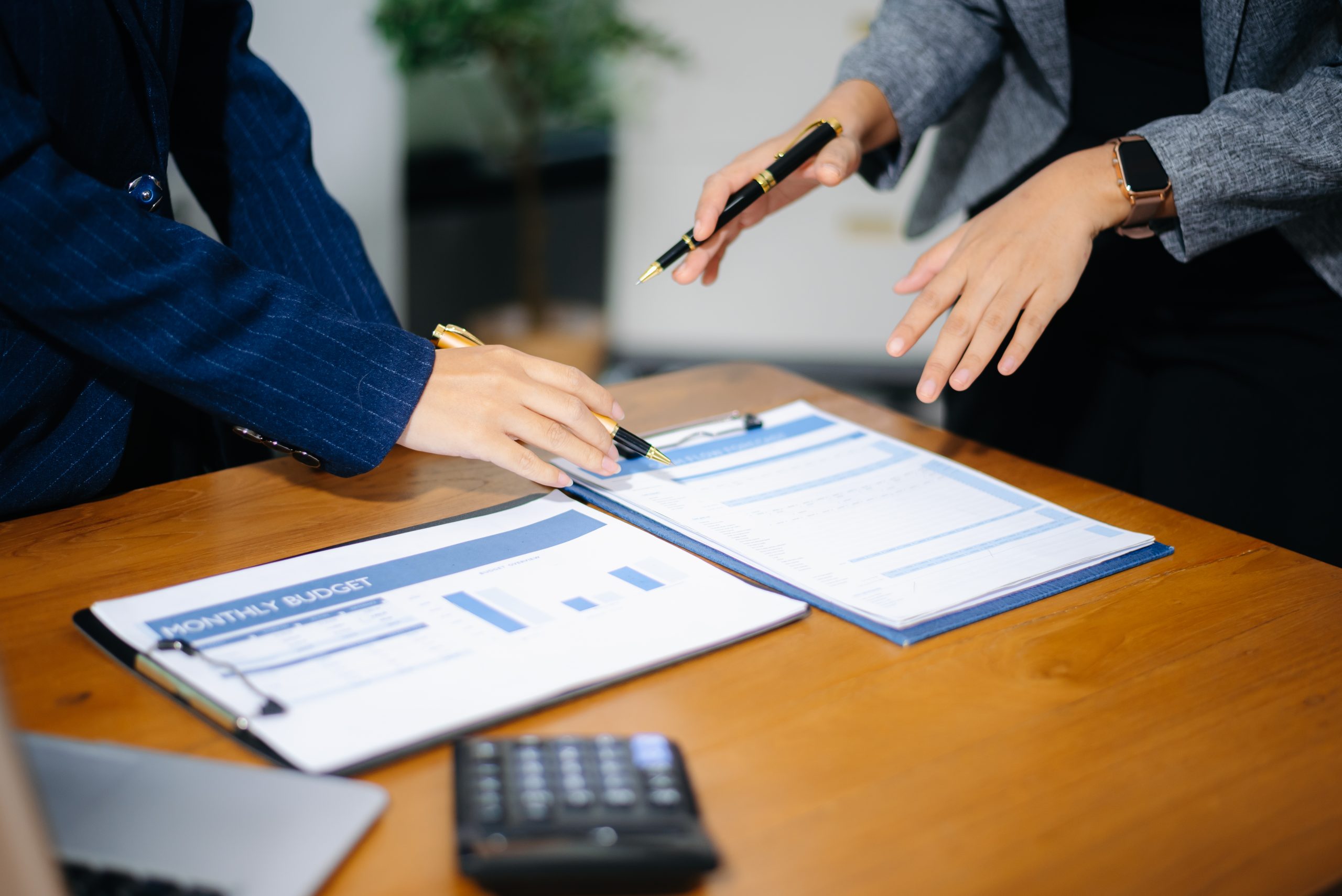 Two people discuss documents and charts on a wooden desk, focusing on ndis audit preparation, with a calculator and laptop nearby.